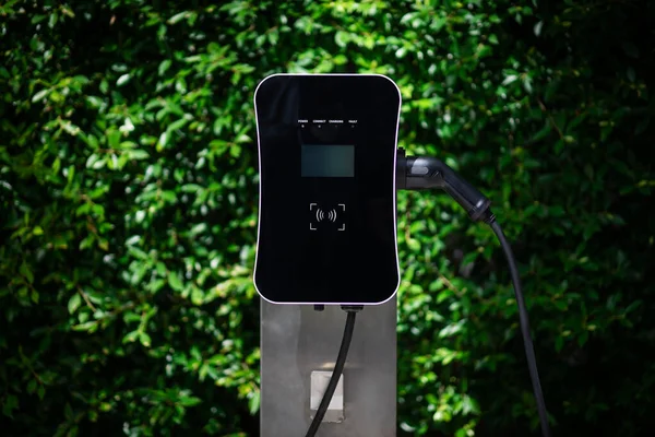 Charging station with greenery foliage background for combination of nature and alternative energy for progressive future renewable energy for electric car. Charger point with connecter device.