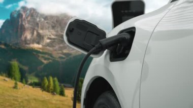 Temiz çevre için temiz enerjinin yol açtığı ilerici elektrikli araba kavramının arka planı olarak dağın tepesinde bulutun zaman kavramının yer aldığı doğal manzara. EV araba şarj istasyonunda şarj oluyor..