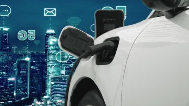 5G Network dijital hologramı ve internet tabelaları gece şehrinin arka planında beliriyor. Çevre koruma kavramı için kablo prizi olan şarj istasyonuna bağlı ilerici elektrikli araç.