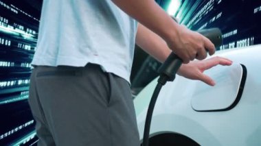 İlerici adam şarj istasyonundan elektrik kablosu kablosuyla şarj ediyor ve Votex 'ten geçen ikili kod teknolojisine sahip. Modern teknolojiyle EV araba konsepti.