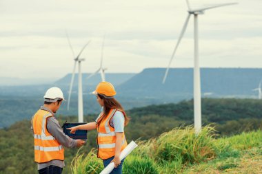 Erkek ve kadın mühendisler kırsal kesimdeki bir tepenin tepesinde ya da dağda rüzgar çiftliğinde çalışıyorlar. Yenilenebilir ve sürdürülebilir enerjinin gelecekteki üretimi için yenilikçi idealler.