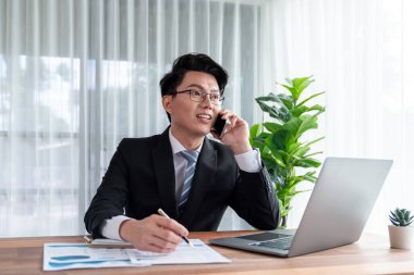 Ofis masasında akıllı telefonuyla bilgisayar başında çalışan bir iş adamı. Akıllı bir yönetici finansal iş verilerini araştırıyor ya da stratejik işler planlıyor, telefonla konuşuyor. Sevinçli.