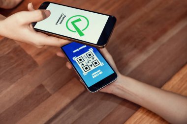 QR kodu parasız ödeme taraması için ekranda gösterilir. Kapalı eller, mobil uygulamadan elektronik işlem yoluyla para aktarmak için akıllı telefonu tutuyor. Hızlı ödeme için barkod teknolojisi. Coşkulu.
