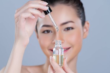 Focus cannabis extracted oil bottle with dropper lid holding by blurred glamorous beautiful asian woman with perfect clean skin and soft smooth makeup in isolated background.