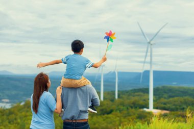 Progressive happy family enjoying their time at wind farm for green energy production concept. Wind turbine generators provide clean renewable energy for eco-friendly purposes.