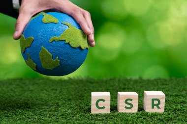 Kâğıt küre ve CSR sembolü küpüyle el ele tutuşan bir iş adamı. CO2 emisyon politikası olmayan çevre dostu yeşil ve etik iş şirketi. Yeşil toplumdan sorumlu kurumsal toplum. Değiştir