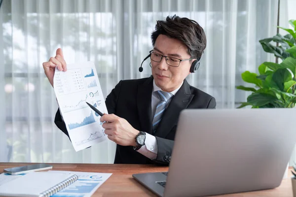 stock image Confident asian telesales businessman work in modern office wearing headphone, presenting BI dashboard analysis to clients and customers in online meeting. Success modern telesales business . Jubilant