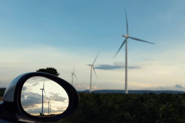 風力発電機からのグリーン 再生可能エネルギーを利用した充電ステーションにおいて 電気自動車のサイドミラーに反射する風力発電機の先進的な未来エネルギーインフラの概念 — ストック写真