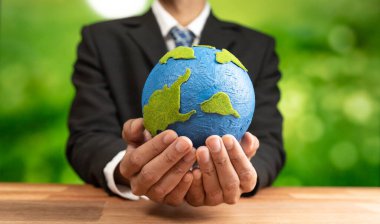 İşadamı temiz enerji ve sıfır CO2 emisyonu kullanarak sürdürülebilir dünya için çevresel farkındalığın sembolü olarak kağıt toprağı elinde tutuyor. Dünya 'yı kurtarmak için yeşil politikası olan çevre dostu bir şirket. Değiştir