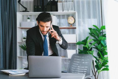 Çalışkan işadamı, ofisindeki dizüstü bilgisayarla cep telefonlu, modern, çalışkan ofis çalışanı yaşam biçimi konsepti olarak çalışırken müşterileriyle telefonda konuşmakla meşgul. Coşkulu