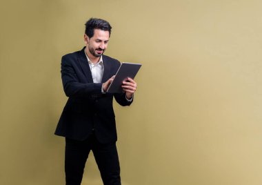 Resmi takım elbiseli kendine güvenen işadamı elinde tabletle sürpriz bir şekilde terfi ya da reklam arıyor. Yüz ifadeleri ve jestler, izole bir arkaplanda heyecan ve şaşkınlığa işaret ediyor. Coşkulu