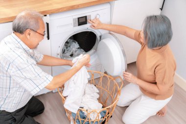 Senior couple working together to complete their household chores at the washing machine in a happy and contented manner. Husband and wife doing the usual tasks in the house.