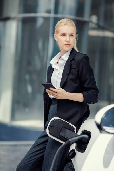 Businesswoman Wearing Black Suit Using Smartphone Leaning Electric Car Recharge — 图库照片