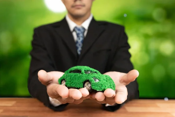 Businessman holding green eco car model in office. Electric vehicle utilized by eco-friendly business for environmental friendly transportation. Corporate responsible with zero CO2 emission. Alter