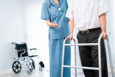 Physiotherapist assists her contented senior patient on folding walker. Recuperation for elderly, seniors care, nursing home.