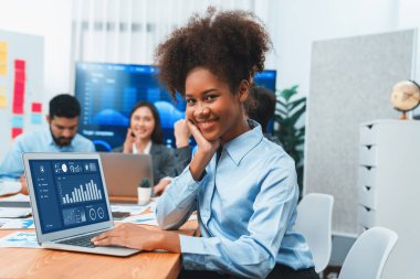 Bir grup ofis çalışanı ile birlikte arka planda ekranda gösterim paneliyle buluşan mutlu Afrikalı genç bir iş kadını portresi. Takım toplantısında kendine güveni tam bir ofis hanımı. Uyum