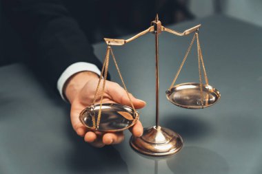 Siyah takım elbiseli bir avukat, altın bir denge, hukuki adalet ve dürüstlük sembolü, mahkemede dengeli ve etik karar verme mekanizması ile birlikte bürosunun masasında dikkatle oturuyor. denge