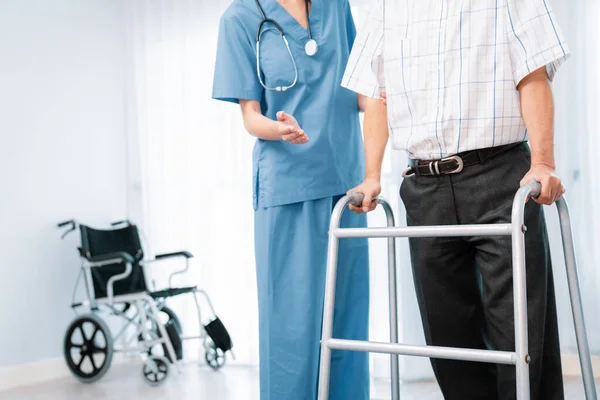 Stock image Physiotherapist assists her contented senior patient on folding walker. Recuperation for elderly, seniors care, nursing home.