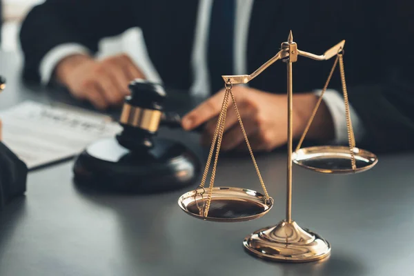 Focus shiny golden balanced scale on blurred background of lawyer colleagues working on desk at law firm office. Scale balance for righteous and equality judgment by lawmaker and attorney. Equilibrium