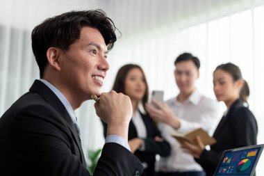 Portrait of focus young successful confident male manager, executive wearing business wear in harmony office arm crossed with blurred meeting background of colleagues, office worker.