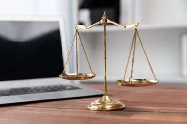 Adalet ve hukuki otoriteyi simgeleyen, hukuk bürosunda dizüstü bilgisayarla birlikte masanın üzerinde duran altın dengeli ölçek, avukat ve yargıcın eşitlik ve adil yargılama kavramını yansıtıyor. denge