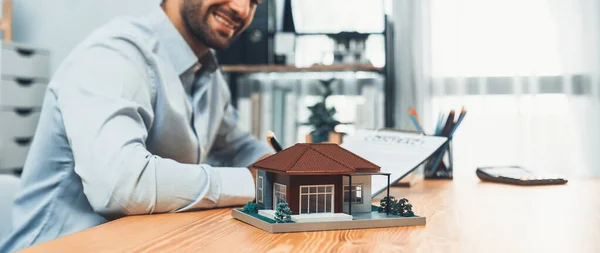 Focus house sample model with blurred satisfied buyer sign house loan or purchase agreement with smile, finalizing the deal. Essential paper for home property ownership with mortgage rate. Fervent