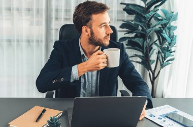 İşadamı laptopuyla çalışıyor ve çalışma masasında kahve içiyor. Akıllı yönetici şirket bilgisayarındaki finansal verileri ve pazarlama planını inceledikten sonra kahve molası veriyor. Varlık