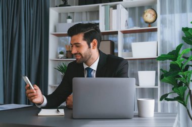 Çalışkan işadamı, ofisindeki dizüstü bilgisayarla cep telefonlu, modern, çalışkan ofis çalışanı yaşam biçimi konsepti olarak çalışırken müşterileriyle telefonda konuşmakla meşgul. Coşkulu