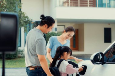 Progressive young parents and daughter with electric vehicle and home charging station. Green and clean energy from electric vehicles for healthy environment. Eco power from renewable source at home.