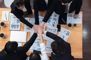 Top view cohesive group of business people join hands together, form circle over table filled with financial report paper. Colleagues working to promote harmony and team building concept in workplace.