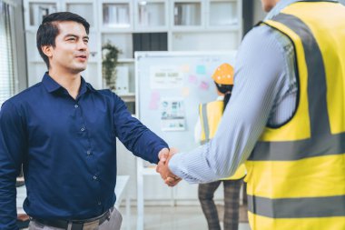 An engineer with a protective vest handshake with an investor in his office. Following a successful meeting, employee and employer form a partnership.