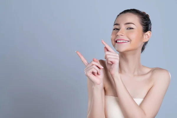 stock image Glamorous beautiful woman with perfect makeup clean skin pointing finger in copyspace isolated background. Promotion indicated by hand gesture concept for skincare product advertisement.