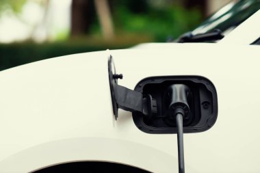 Closeup electric vehicle plugged-in with cable from charging point powered for progressive concept by alternative clean energy rechargeable EV car at home charging station.