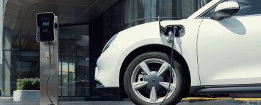 Progressive electric vehicle recharging battery at charging station powered by sustainable clean energy at city residential area. Eco-friendly vehicle concept.