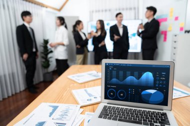 Focus laptop monitor display dashboard report by business intelligence, analyzed financial data for planning market strategy with blur background of standing office worker discussing in harmony office