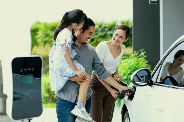 stock image Progressive young parent teach daughter how to recharge or refuel EV car at home charging station. Green and clean energy from electric vehicle for healthy environment. Eco power from renewable source