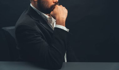 Resmi siyah takım elbiseli bir iş adamı ya da avukat izole edilmiş siyah arka planda oturuyor. Otorite ve ciddi jestleri olan bir adam kavramı. denge
