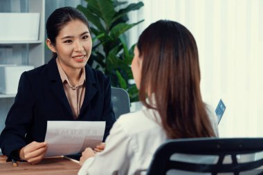 İki Asyalı kadın ofiste iş görüşmesi yapıyor. Başvuranlar özgeçmişi ve iş başvurusu hakkında konuşurken resmi takım giyerler. Muhabir olumlu ve konuşkan bir şekilde sorgulama talep ediyor. Coşkulu.