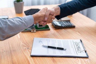 Ev kredisi anlaşmasını el sıkışma, alıcı ve emlakçı ile sonuçlandırmak mülkiyet sahipliğinin başarısını memnuniyet duygusuyla kutluyor. Yeni ev sahibi brokerla el sıkışıyor. Varlık