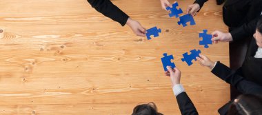 Top view businesspeople and colleagues in formal wear putting jigsaw puzzles together over meeting table with financial report papers in harmony office for team building concept.
