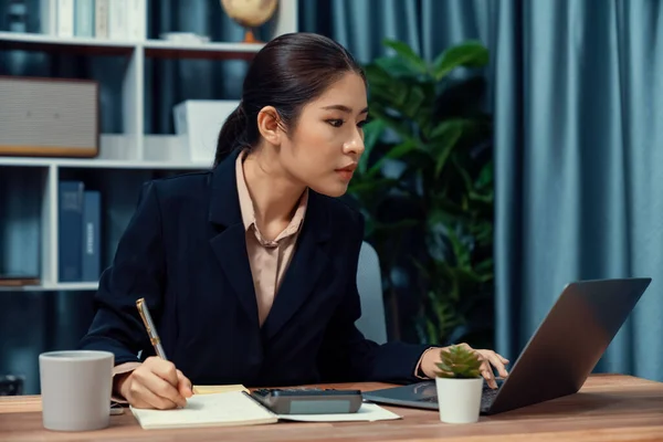 stock image Young asian businesswoman is diligently working and taking notes in her modern office workspace, demonstrating professionalism as attractive and diligent office lady. Enthusiastic