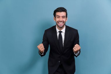 Siyah takım elbise giymiş heyecanlı ve mutlu iş adamı, başarılı bir iş tanıtımı, enerji ve neşe sonrasında, münzevi bir arka planda kutlama jesti olarak kolunu kaldırdı. Coşkulu