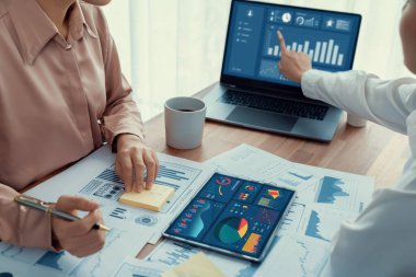 Analist ekip arkadaşı dijital gösterge panelinde finansal verileri tartışır, grafikleri dizüstü bilgisayar ve tablet ekranda analiz eder. Modern ofis pazarlama planlamak için iş zekasını kullanır. Coşkulu.