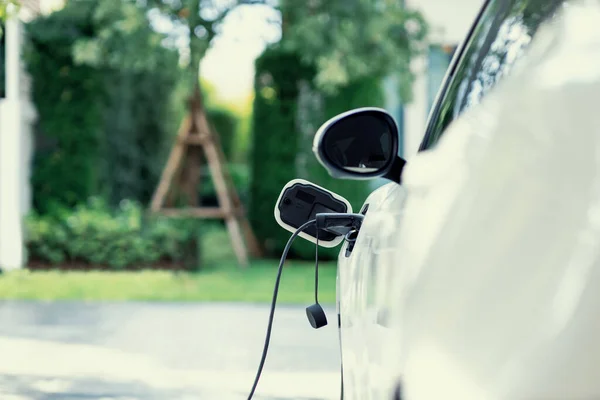 Stock image Closeup electric vehicle plugged-in with cable from charging point powered for progressive concept by alternative clean energy rechargeable EV car at home charging station.