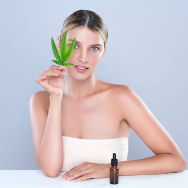 Alluring portrait of beautiful woman in isolated holding green leaf with marijuan extracted bottle for skincare treatment product. Cannabis CBD oil for cosmetology and beauty concept.