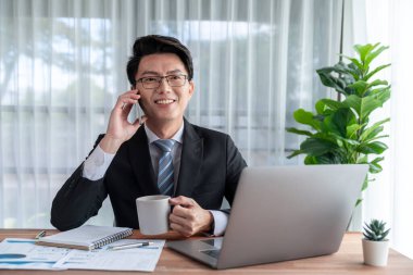 Ofis masasında akıllı telefonuyla bilgisayar başında çalışan bir iş adamı. Akıllı bir yönetici finansal iş verilerini araştırıyor ya da stratejik işler planlıyor, telefonla konuşuyor. Sevinçli.