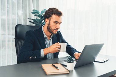 Siyah takım elbiseli bir iş adamı çalışma masasında dizüstü bilgisayarla çalışıyor. Akıllı yönetici finansal verileri araştırıyor ve modern işyerindeki kurumsal dizüstü bilgisayarlarda pazarlama stratejisi planlıyor. Varlık