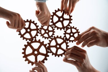 Hand holding wooden gear by businesspeople wearing suit for harmony synergy in office workplace concept. Isolated background. Bottom view of people hand make chain of gear into collective unity symbol