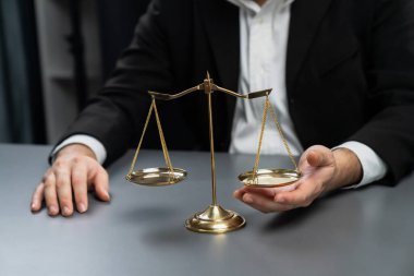 Siyah takım elbiseli bir avukat, altın bir denge, hukuki adalet ve dürüstlük sembolü, mahkemede dengeli ve etik karar verme mekanizması ile birlikte bürosunun masasında dikkatle oturuyor. denge