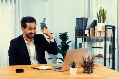 Siyah takım elbise giymiş heyecanlı ve mutlu bir iş adamı başarılı bir iş tanıtımı, enerji ve neşe kazandıktan sonra ofis masasında kutlama jesti olarak elini kaldırır. Coşkulu
